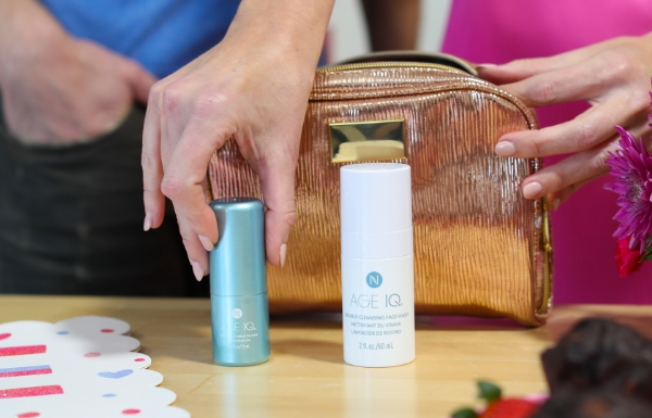 Lifestyle shot of a woman placing the Age IQ Travel Minis Cleanser & Day Cream Combo bottles in front of a travel purse on a wooden table.